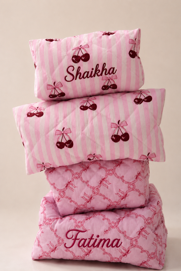 Stack of pink pouches with decorative patterns and names 'Shaikha' and 'Fatima'.