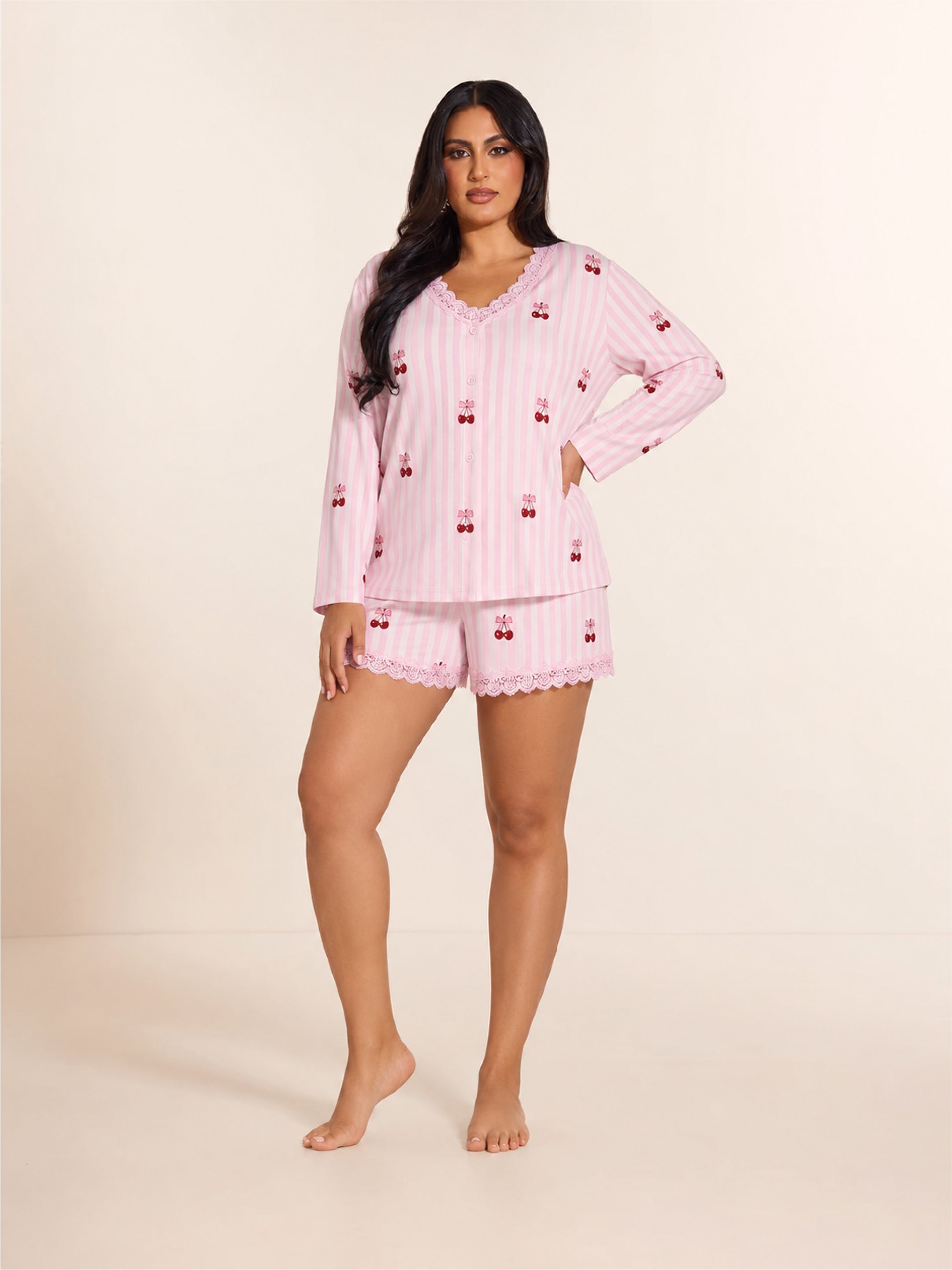 Woman wearing a pink pajama set with cherry pattern on a beige background