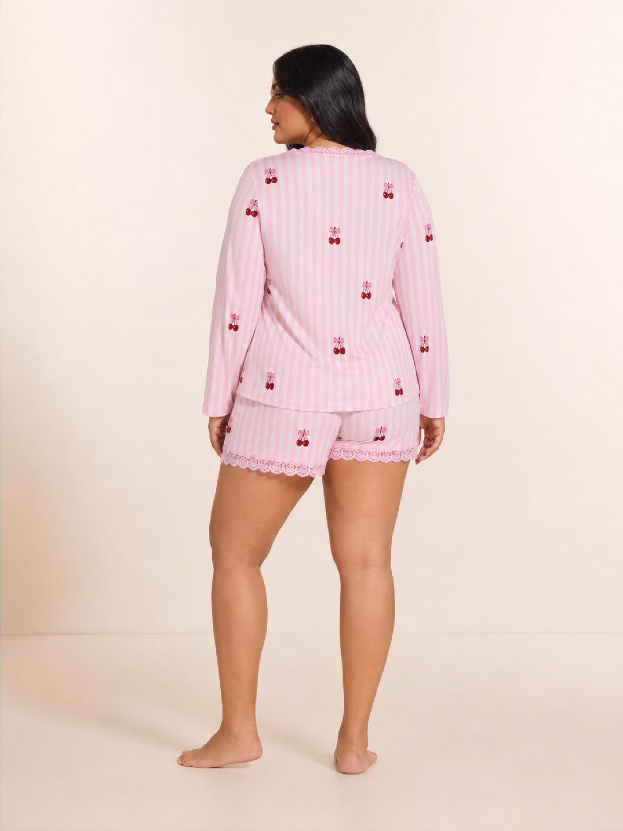 Woman wearing a pink pajama set with cherry pattern on a beige background