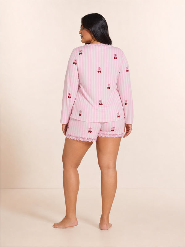 Woman wearing a pink pajama set with cherry pattern on a beige background