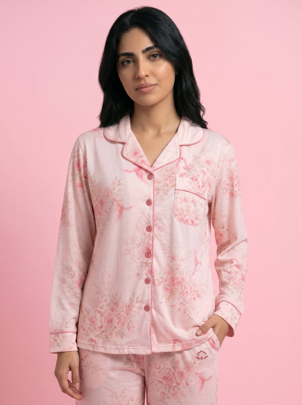 A woman modeling a light pink long-sleeve pajama set with a darker pink floral pattern, standing against a solid pink background.
